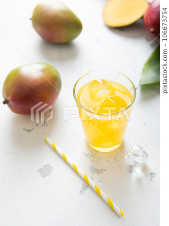 Glass of mango juice with straw and fresh raw organic mangoes on light background.Top view. 106673754
