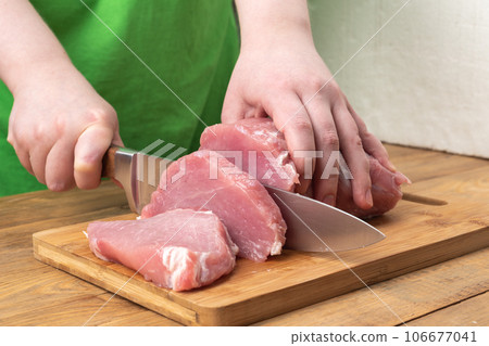 A girl cuts pork meat into pieces using a knife on a cutting board. 106677041