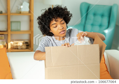 African girl unpacking delivery looking in box. Happy woman opening carton box. Female getting parcel looking at delivered goods items. Satisfied client positive feedback quick express deliver 106677064