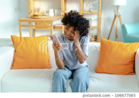 Excited happy young black african american woman holding cell phone laughing feeling joy getting mobile message. Overjoyed girl laughing aloud sitting on couch watching funny video reading news Excited happy young black african american woman holding cell phone laughing feeling joy getting mobile message. Overjoyed girl laughing aloud sitting on couch watching funny video reading news 106677065