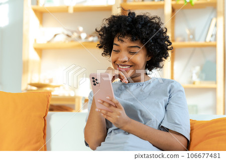 Excited happy young black african american woman holding cell phone laughing feeling joy getting mobile message. Overjoyed girl laughing aloud sitting on couch watching funny video reading news 106677481