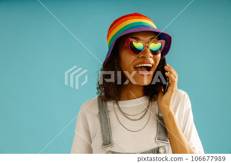 Positive woman in rainbow cap talking by mobile phone standing over blue studio background 106677989