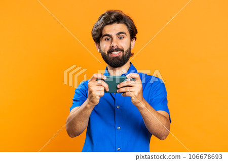 Worried funny addicted tourist guy enthusiastically playing drive racing video game on mobile phone 106678693