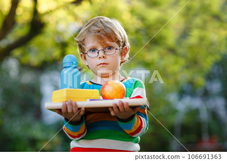 Confused upset little preschool boy with books, apple and drink bottle on his first day to elementary school. Sad child, student with glasses, outdoors. Back to school, fear, education concept. Confused upset little preschool boy with books, apple and drink bottle on his first day to elementary school. Sad child, student with glasses, outdoors. Back to school, fear, education concept. 106691363