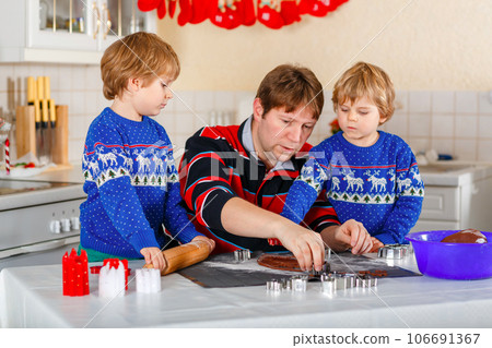 Two little preschool boys and father baking gingerbread cookies. Happy siblings, children and their dad, man in xmas sweaters. Kitchen decorated for Christmas. Christmas family activity Two little preschool boys and father baking gingerbread cookies. Happy siblings, children and their dad, man in xmas sweaters. Kitchen decorated for Christmas. Christmas family activity 106691367