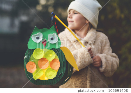 Little preschool kid girl holding selfmade traditional owl lanterns with candle for St. Martin procession. child happy about children and family parade in kindergarten. German tradition Martinsumzug Little preschool kid girl holding selfmade traditional owl lanterns with candle for St. Martin procession. child happy about children and family parade in kindergarten. German tradition Martinsumzug 106691408