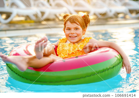 Happy little girl with inflatable toy ring float in swimming pool. Little preschool child learning to swim and dive in outdoor pool of hotel resort. Healthy sport activity and fun for children. Happy little girl with inflatable toy ring float in swimming pool. Little preschool child learning to swim and dive in outdoor pool of hotel resort. Healthy sport activity and fun for children. 106691414