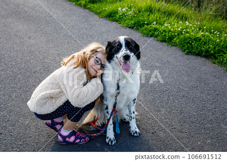Little preschool girl walking with her dog. Cute kid and family pet in nature, fields and forest in late summer. Love and friendship between child and dog. Having fun together. 106691512