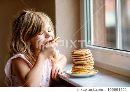 Little happy preschool girl with a large stack of pancakes for breakfast. Positive child eating healthy homemade food in the morning. Little happy preschool girl with a large stack of pancakes for breakfast. Positive child eating healthy homemade food in the morning. 106691521