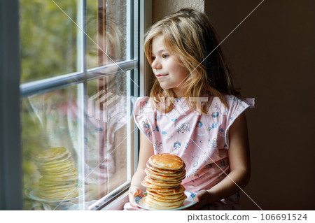 Little happy preschool girl with a large stack of pancakes for breakfast. Positive child eating healthy homemade food in the morning. 106691524