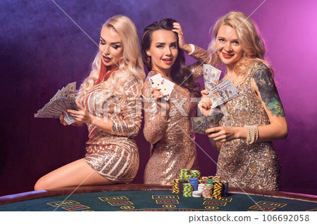 Beautiful girls with a perfect hairstyles and bright make-up are posing standing at a gambling table. Casino, poker. 106692058