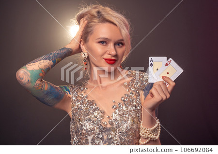 Blonde woman with a beautiful hairstyle and perfect make-up is posing with playing cards in her hands. Casino, poker. Blonde woman with a beautiful hairstyle and perfect make-up is posing with playing cards in her hands. Casino, poker. 106692084