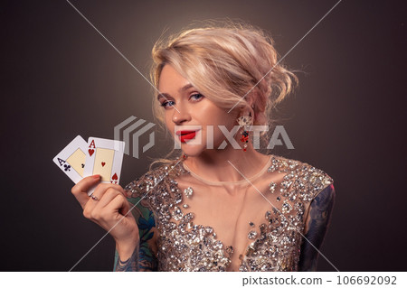 Blonde woman with a beautiful hairstyle and perfect make-up is posing with playing cards in her hands. Casino, poker. 106692092