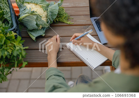 Close up of woman farm owner making notes in notepad with vegetables on background 106693368