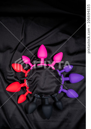 A set of silicone anal plugs in different colors and sizes on a black silk sheet.  106694835