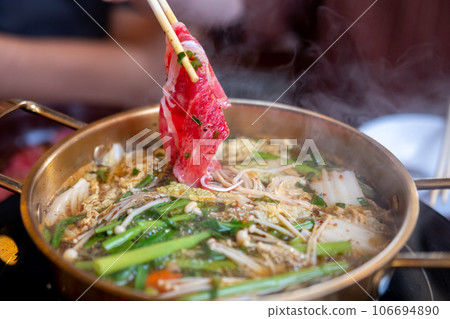 Chopstick holding sliced meat. hot pot with thick soup. 106694890