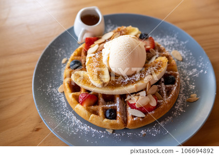 Waffle with ice cream and blueberry, strawberry, banana and honey served on plate 106694892