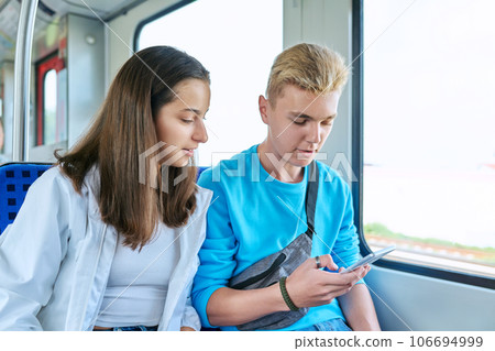 Teenage guy and girl commuter train passengers sitting together looking at smartphone 106694999