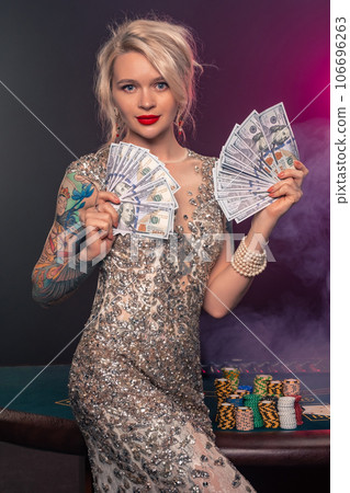 Blonde woman with a beautiful hairstyle and perfect make-up is posing with some money in her hands. Casino, poker. Blonde woman with a beautiful hairstyle and perfect make-up is posing with some money in her hands. Casino, poker. 106696263