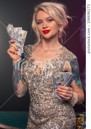 Blonde woman with a beautiful hairstyle and perfect make-up is posing with some money in her hands. Casino, poker. Blonde woman with a beautiful hairstyle and perfect make-up is posing with some money in her hands. Casino, poker. 106696273