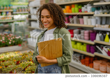 Smiling female gardener standing with clipboard on background of botanic shop  106696387
