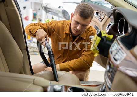 Man vacuuming driver seat in car using portable blower machine Man vacuuming driver seat in car using portable blower machine 106696941