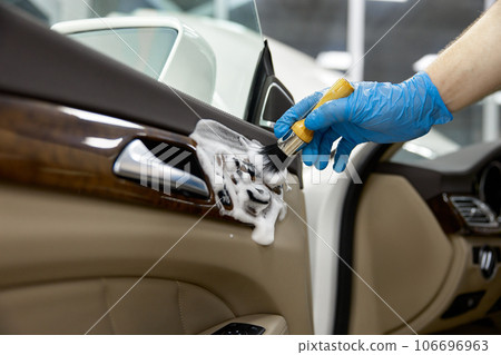 Car detailing service, closeup worker cleaning washing leather door parts with brush 106696963