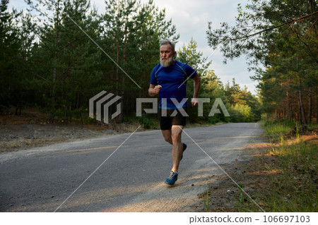Senior man jogger performing exercise outside among countryside road Senior man jogger performing exercise outside among countryside road 106697103