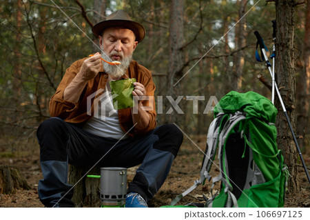 Relaxed senior man hiker eating food taking break after touristic trip in forest Relaxed senior man hiker eating food taking break after touristic trip in forest 106697125