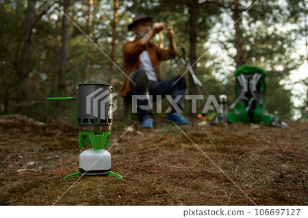 Elderly man hiker cooking food in forest, closeup view on portable gas burner Elderly man hiker cooking food in forest, closeup view on portable gas burner 106697127