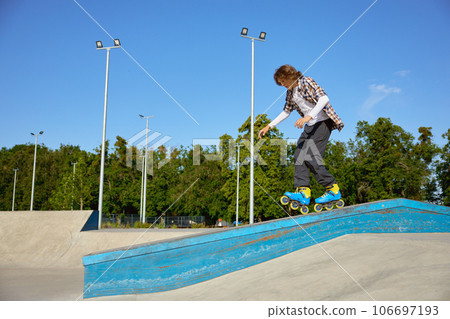 Young guy wearing inline skates doing balancing stunt at skateboard park 106697193