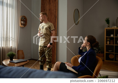 Military man in camouflage uniform standing nearby window at therapy session 106697212
