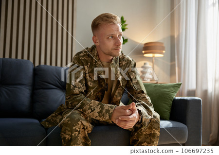 Depressed veteran wearing military uniform sitting on couch feeling upset Depressed veteran wearing military uniform sitting on couch feeling upset 106697235