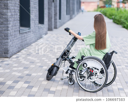 A woman in a wheelchair with an assistive device for manual control. Electric handbike. A woman in a wheelchair with an assistive device for manual control. Electric handbike. 106697383