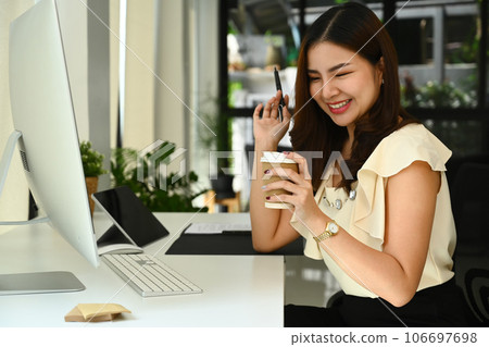 Pleasant businesswoman holding paper cup of coffee and working at modern workplace 106697698