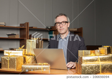 Mature businessman in blue suit, he is sitting by the table working on the laptop Mature businessman in blue suit, he is sitting by the table working on the laptop 106698094