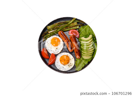 A delicious nourishing breakfast with fried eggs, sausages, asparagus, tomatoes, avocado, spices and herbs 106701296