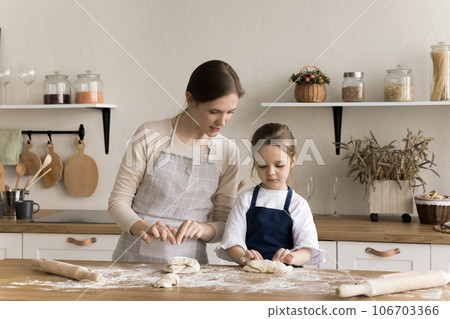 Caring mom teaching cute toddler girl in apron to cook Caring mom teaching cute toddler girl in apron to cook 106703366