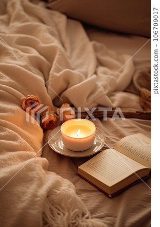 an open book and a lit candle on a bed with a white blanket in the photo is taken from above 106709017