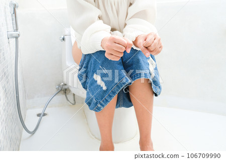Woman sitting on the toilet bowl in the bathroom. She has stomach ache. Poor digestive system. Constipation. Diarrhea. Food poisoning. Health and medicine. Woman sitting on the toilet bowl in the bathroom. She has stomach ache. Poor digestive system. Constipation. Diarrhea. Food poisoning. Health and medicine. 106709990