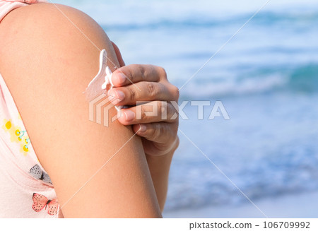 A woman is applying sunscreen and skin care to protect her skin from UV rays. She is applying sunscreen on her shoulder . The sun symbol is a very sunny background. Health and skin care concept A woman is applying sunscreen and skin care to protect her skin from UV rays. She is applying sunscreen on her shoulder . The sun symbol is a very sunny background. Health and skin care concept 106709992