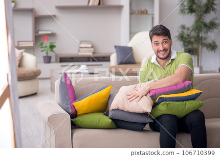 Young man with a lot of pillows sitting on the sofa Young man with a lot of pillows sitting on the sofa 106710399