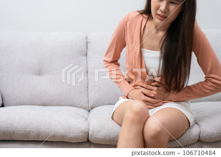 Sick Asian Woman Suffering From Acute Abdominal Pain in the abdomen due to menstruation period, PMS.  Sitting On Couch, stomachache from food poisoning, abdominal pain, digestive problem, gastritis 106710484