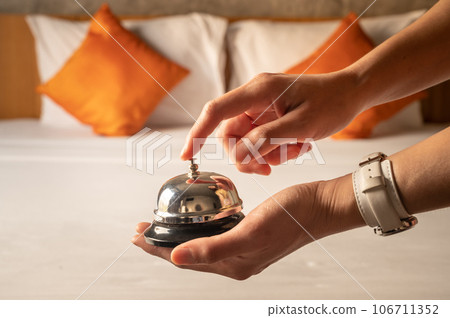 Close-up of guest hand holding and ringing hotel bell in hotel bedroom. Hotel bell is normally use to call staff service and staff can help guests with any queries that they may have. 106711352