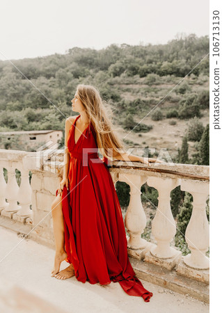 Woman red dress. Summer lifestyle of a happy woman posing near a fence with balusters over the sea. Woman red dress. Summer lifestyle of a happy woman posing near a fence with balusters over the sea. 106713130