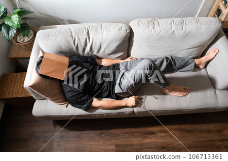 Man with mental health problem lying on comfortable couch and covering face with book to sleeping Man with mental health problem lying on comfortable couch and covering face with book to sleeping 106713361
