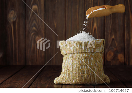 sea salt falling from scoop in bag on wooden table 106714657
