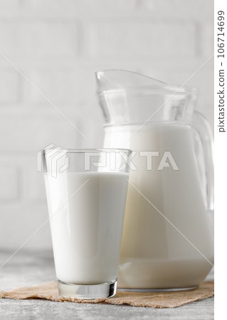 jug and glass of milk on table with white brick wall as background 106714699
