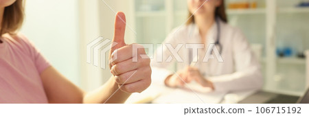 Woman patient shows thumbs up while sitting near female doctor in clinic. 106715192