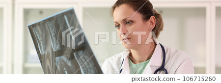 Female doctor examining x-ray scan film of patient while sitting at hospital. 106715260